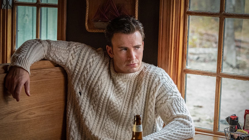 Chris Evans wears off white knitted jumper and sits next to window in wooden diner booth with beer and table setting.