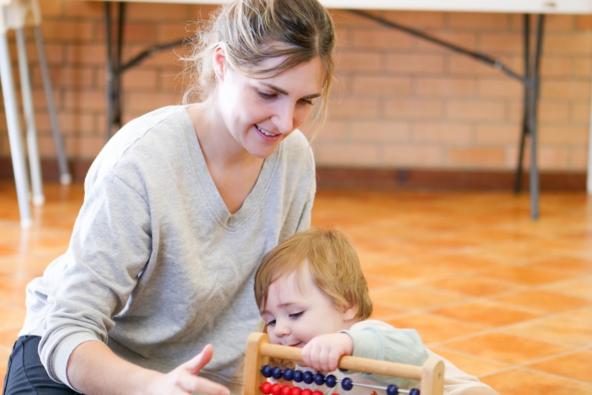 A woman and a baby on the floor playing with an abacus