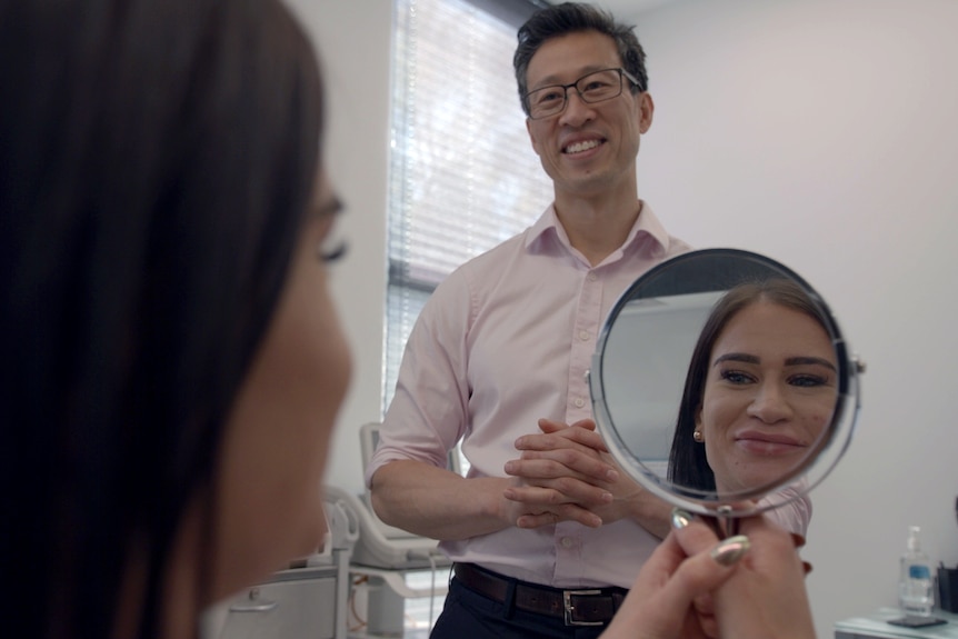 woman looks into mirror with Dr smiling at her