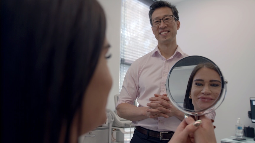 woman looks into mirror with Dr smiling at her