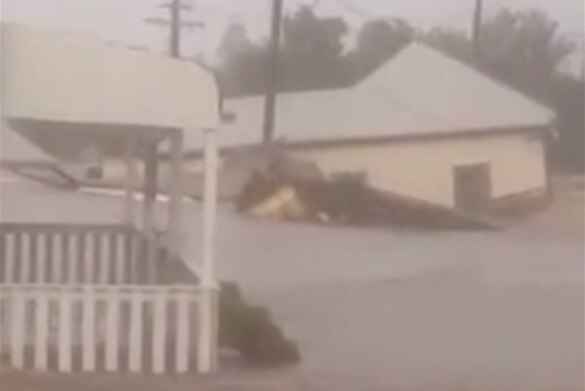 Timber house floats away with debris in brown floodwaters.