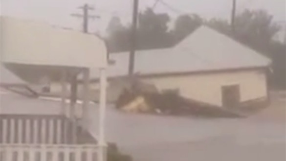 Timber house floats away with debris in brown floodwaters.
