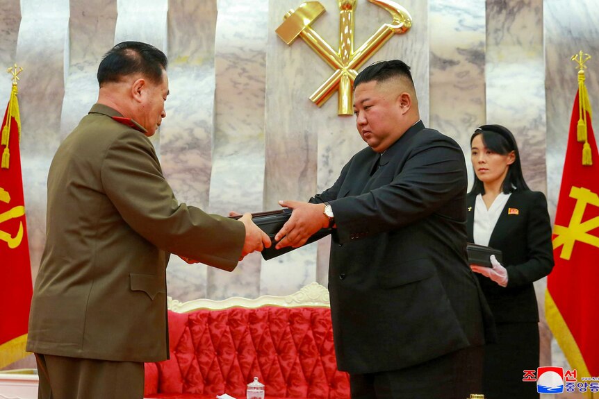 Kim Jong-un handing a box to a man in uniform while his sister looks on