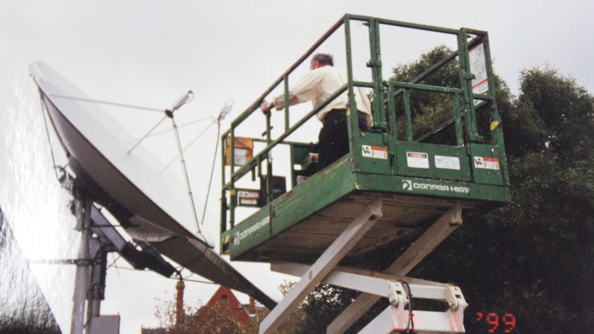 A man on a crane works on ABC Gippsland's satellite