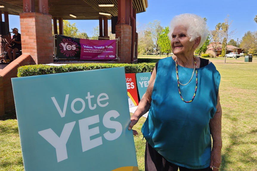 First nations female elder stands outside holding campaign sign that says 'vote yes'