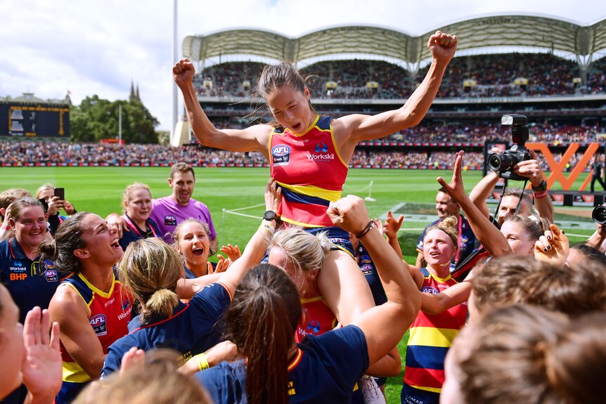 Sophie Li sits on a teammates shoulders while the rest of the Adelaide Crows gather around them