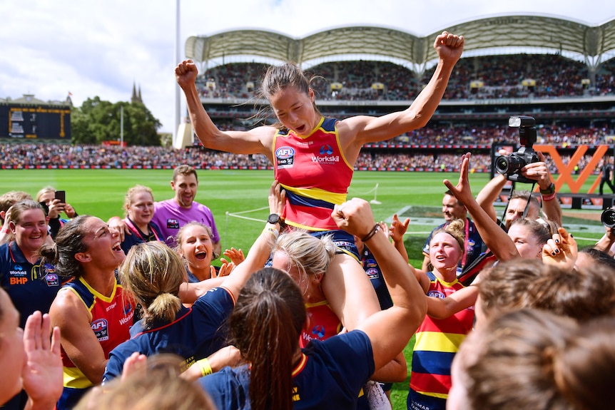 Sophie Li sits on a teammates shoulders while the rest of the Adelaide Crows gather around them