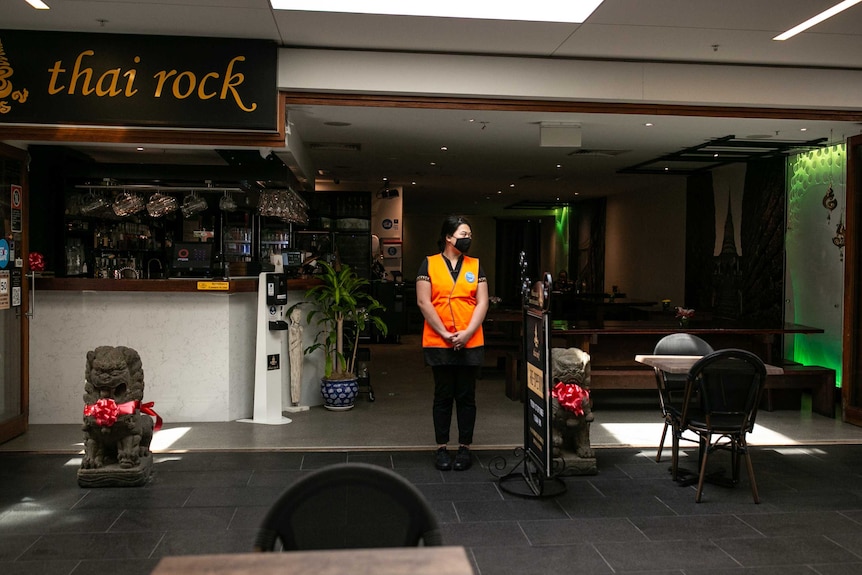 A woman with a face mask stands between several empty tables