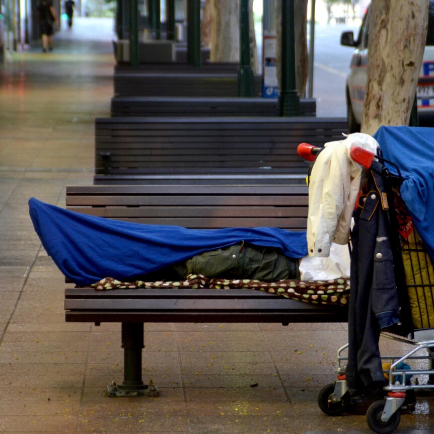 A homeless person lies on a seat on Adelaide Street in the Brisbane CBD.