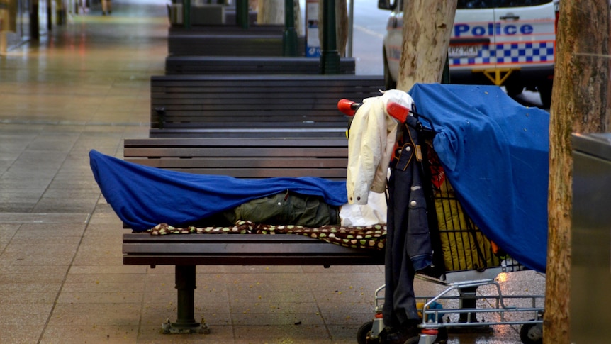 A homeless person lies on a seat on Adelaide Street in the Brisbane CBD.