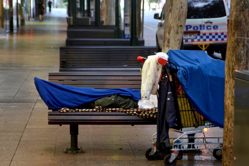 A homeless person lies on a seat on Adelaide Street in the Brisbane CBD.