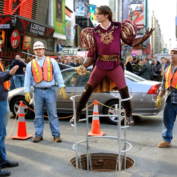 A photograph of actor James Marsden dressed as a prince, brandishing a sword at three tradespeople in Times Square.