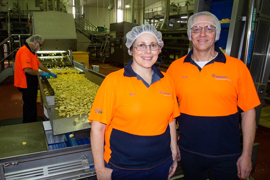 Woman and man standing in front of potato chip factory production line. 