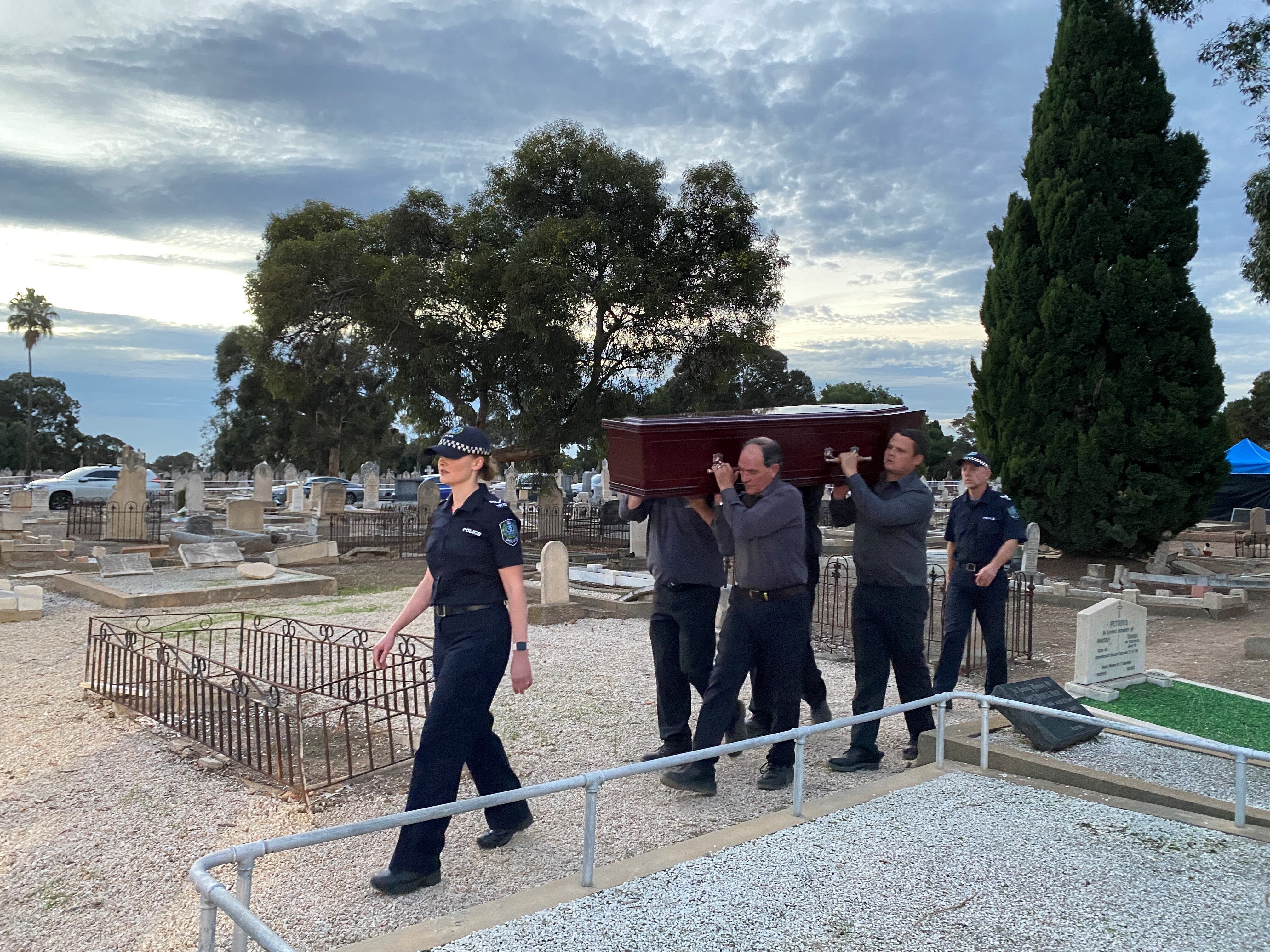 SA Police officers escort a coffin in a cemetery.
