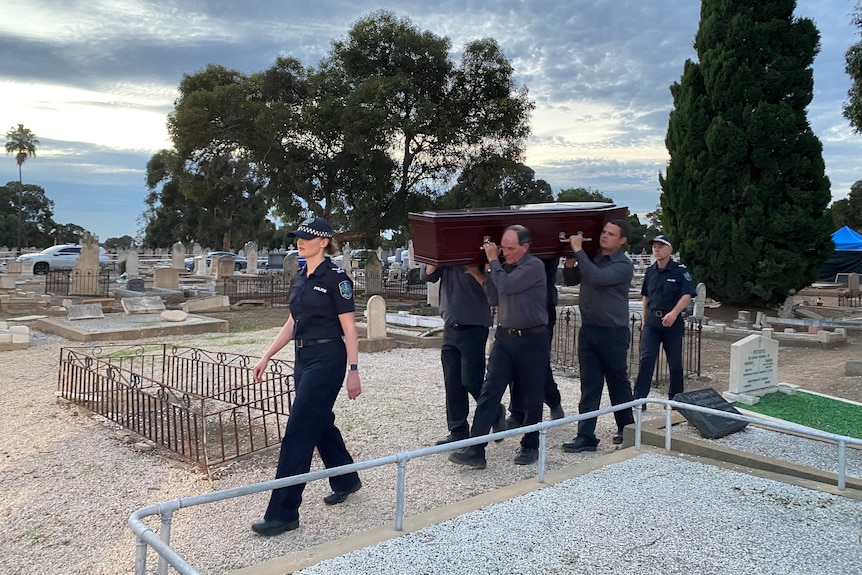 SA Police officers escort a coffin in a cemetery.