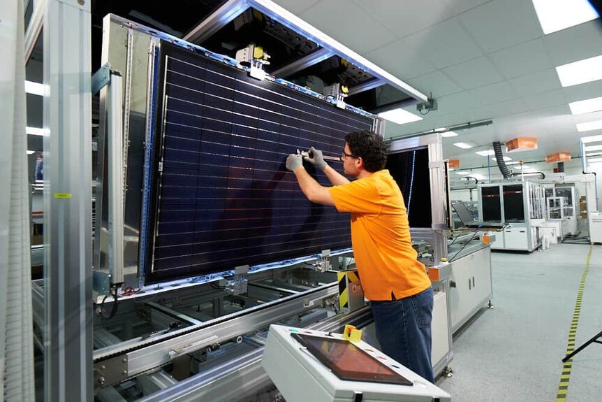 A man in orange uniform with a solar panel on an assembly line