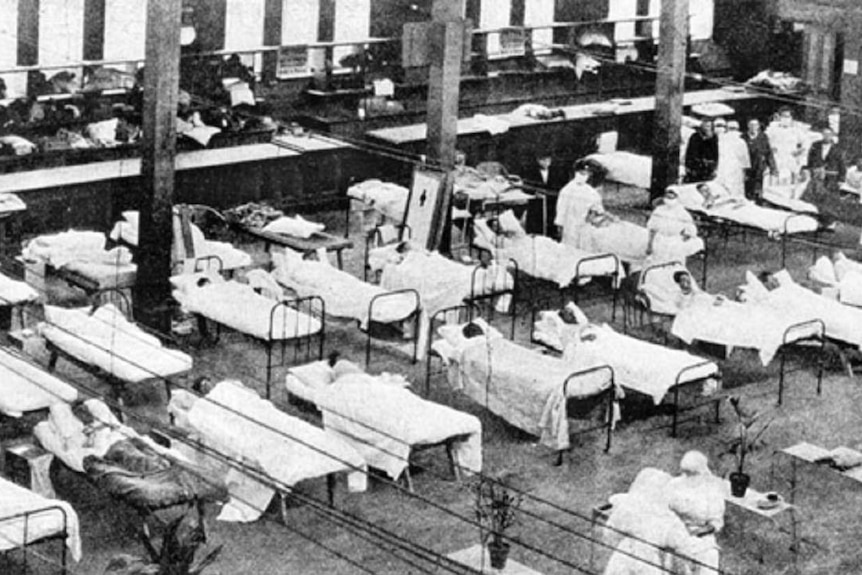 Dozens of beds are laid out inside the Great Hall of the Royal Exhibition Building, in a black and white photograph.