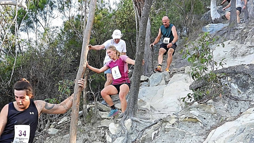 Three male and one female run down the steep rocky track of the mountain.