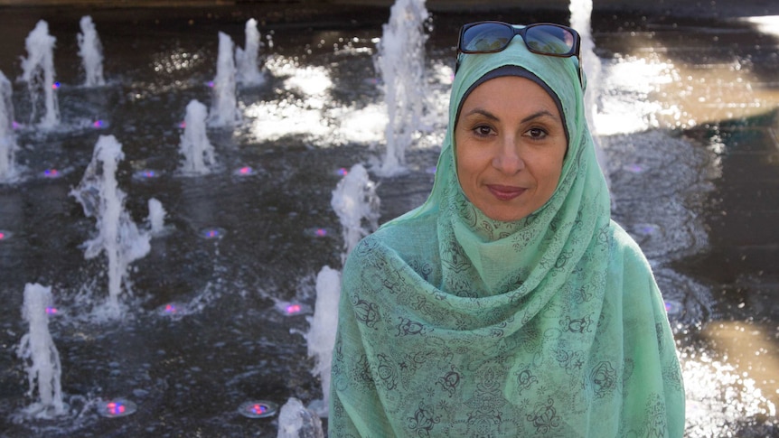 Woman Gada Omar wearing hijab and standing in front of fountain.