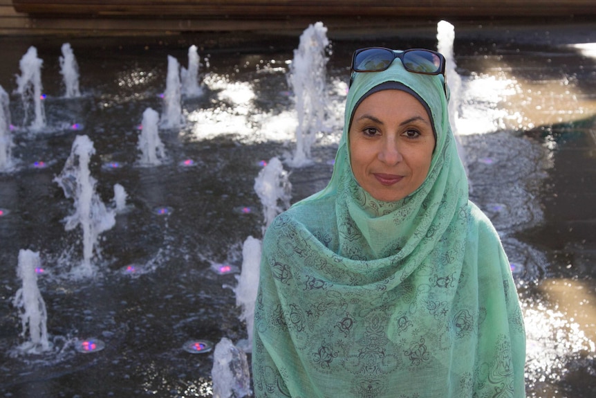 Woman Gada Omar wearing hijab and standing in front of fountain.