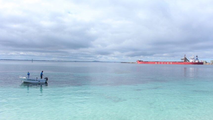 A ship at Esperance Port, as two men fish from a boat in the foreground