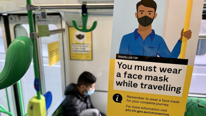 A sign reads 'You must wear a face mask while travelling' on the inside of a tram.