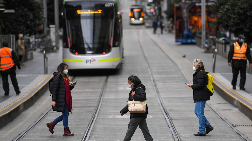 People wearing face masks cross the road in front of a tram in Melbourne.