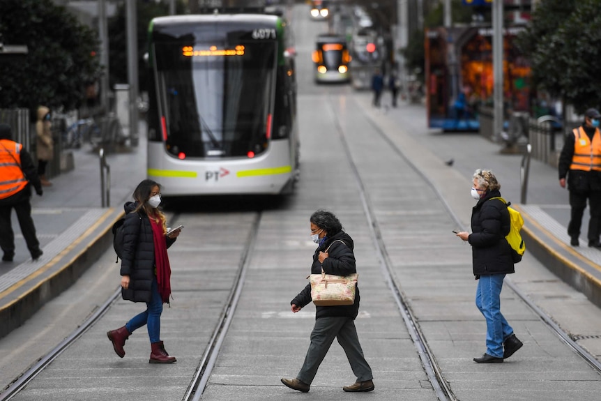 People wearing face masks cross the road in front of a tram in Melbourne.