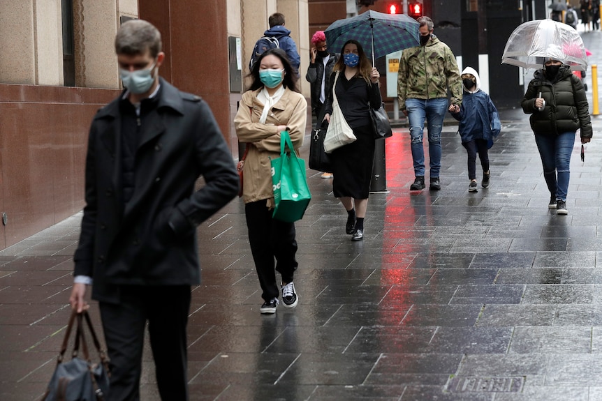Masked pedestrians walk down a rainy street in Sydney