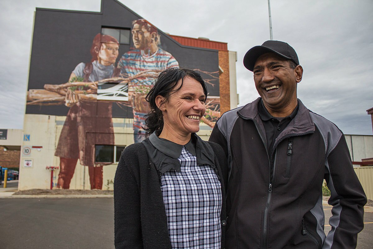 A couple stand smiling in front of a street mural