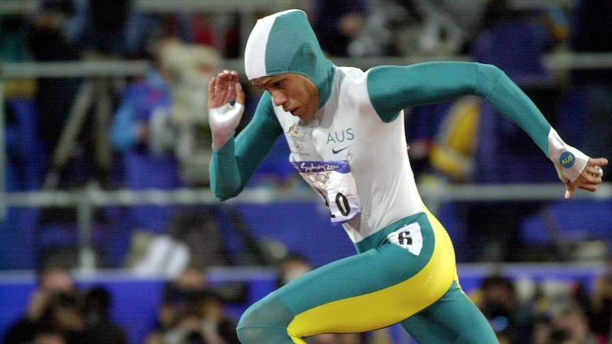 An Australian athlete, wearing a green, white and gold bodysuit, runs with her head down.