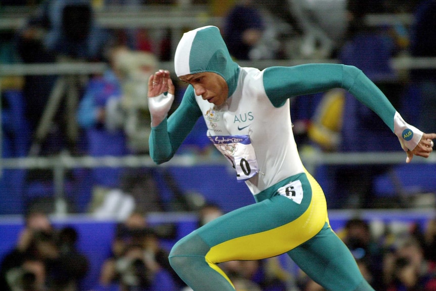 An Australian athlete, wearing a green, white and gold bodysuit, runs with her head down.