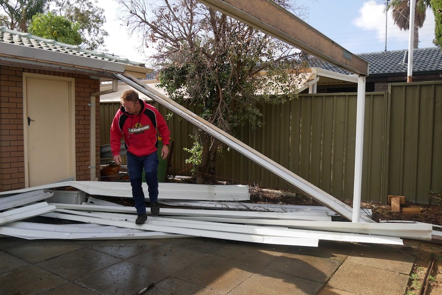 Mr Edwards steps over fallen pieces of metal from what looks like it was once a car port.