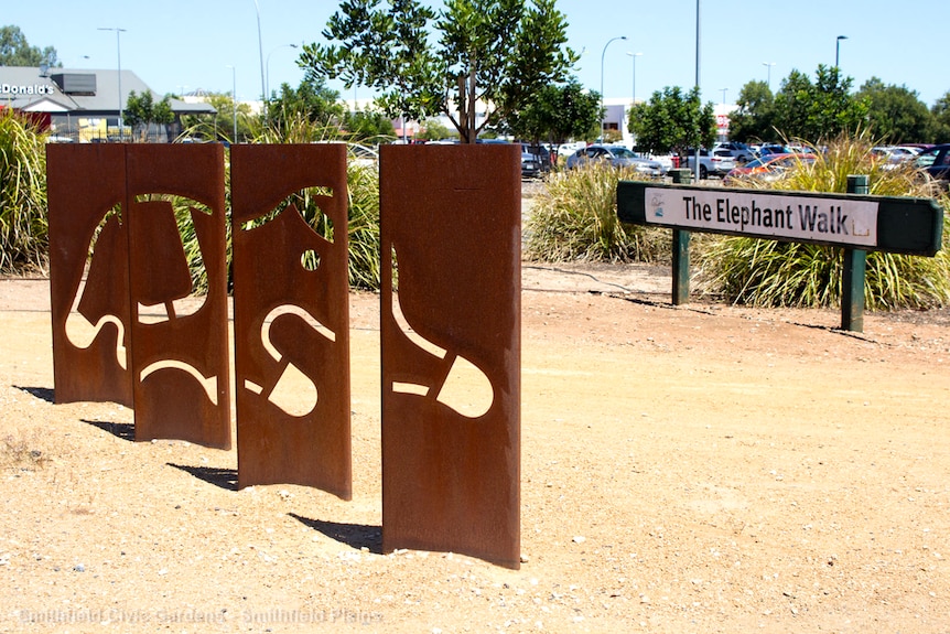 A metallic sculpture with the outline sits adjacent a sign reading elephant walk