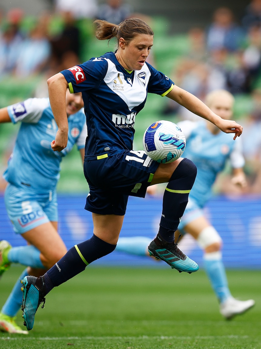 A soccer player wearing navy blue controls the ball on her knee