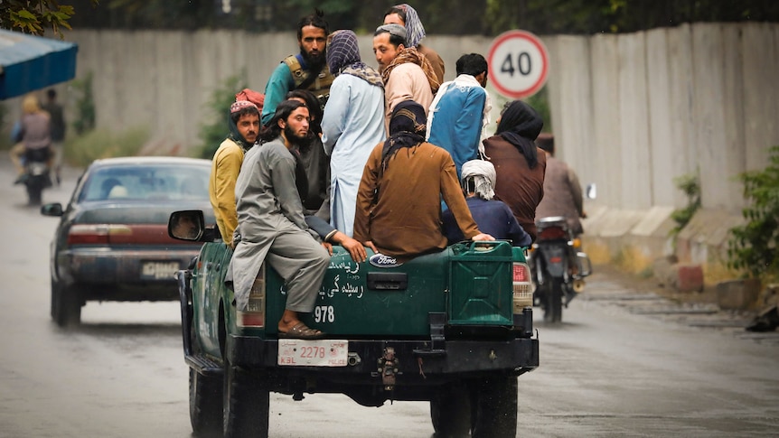 A group of men in traditional Afghan garb piled into the tray of a ute driving down a street