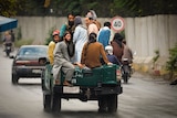 A group of men in traditional Afghan garb piled into the tray of a ute driving down a street