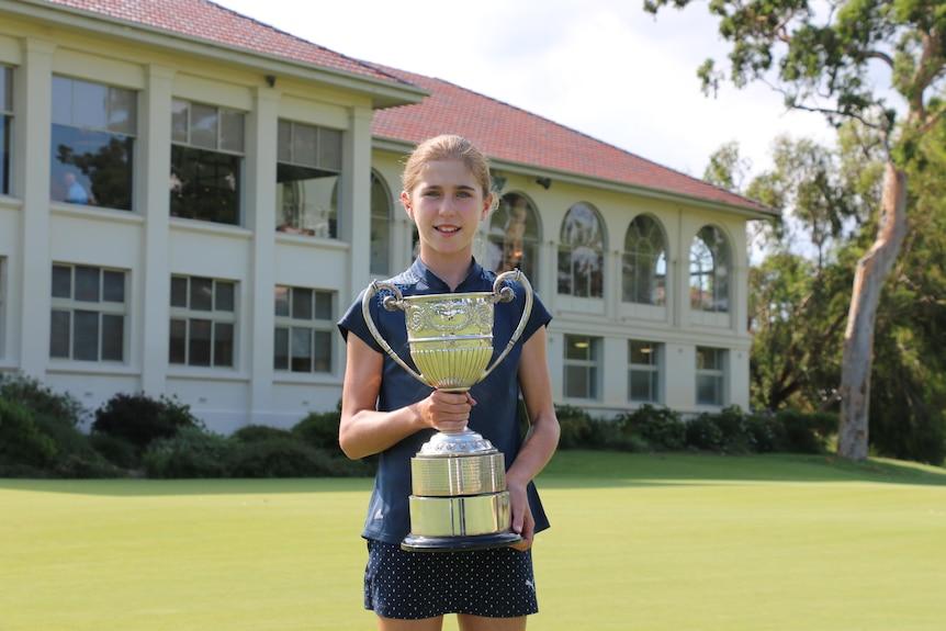 A young woman holds a trophy on a golf course.