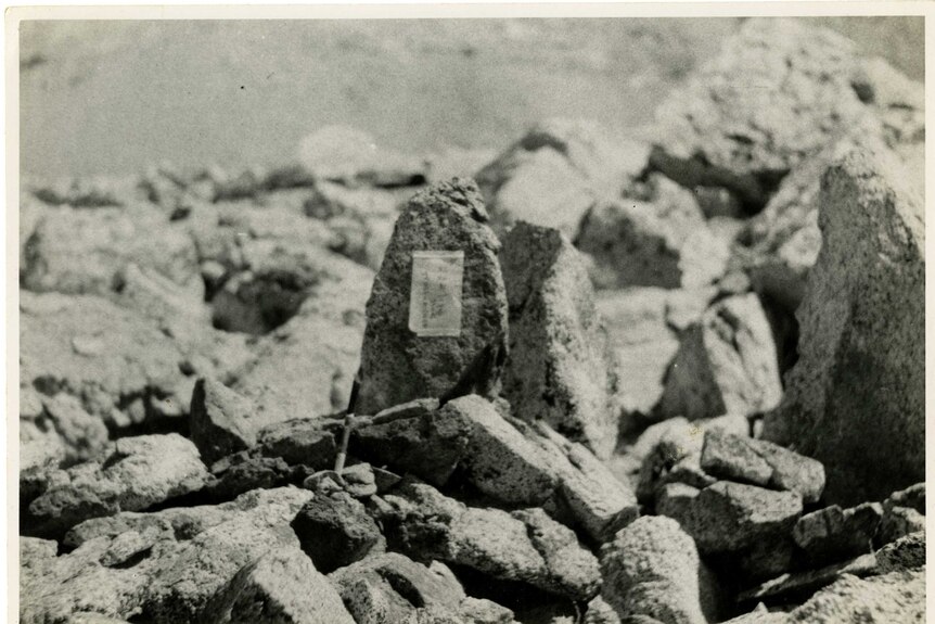 A black and white photo of rocks piled together, one has a paper note attached with Japanese characters on it.