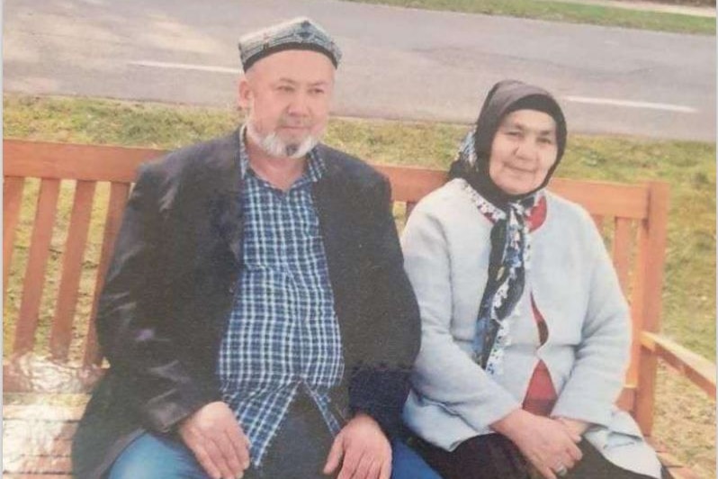 An elderly man and women smile as they sit closely together on a park bench.