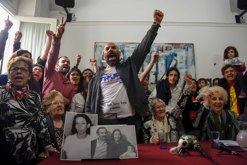 A group of people raise their arms and cheer during a press conference about Argentina's missing grandchildren.