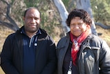 a man wearing a blue polo and a balck jacket stands next to a woman wear a grey jacket and red scarf 