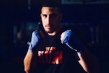 A young male boxer looks directly into the camera, fists up. 