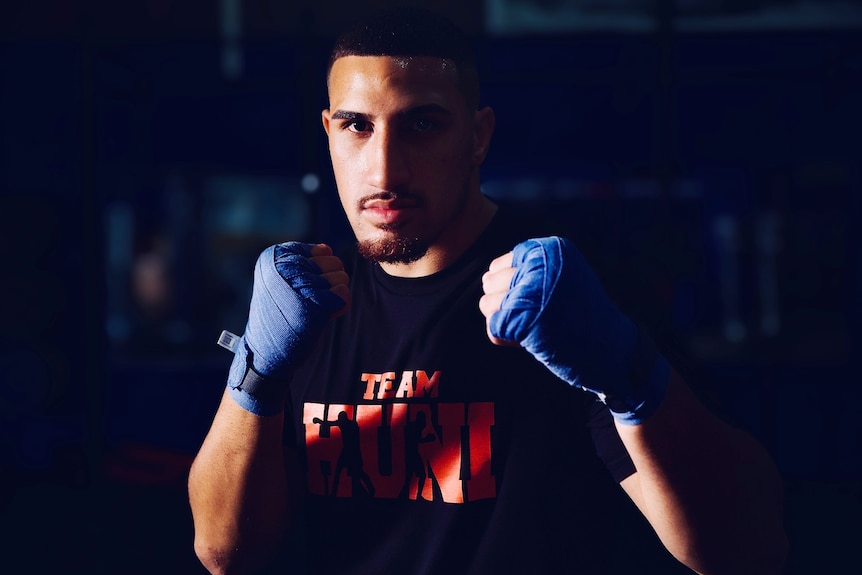 A young male boxer looks directly into the camera, fists up. 