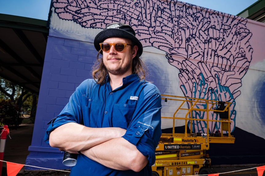 a man wearing a blue shirt in front of hands painted on a wall