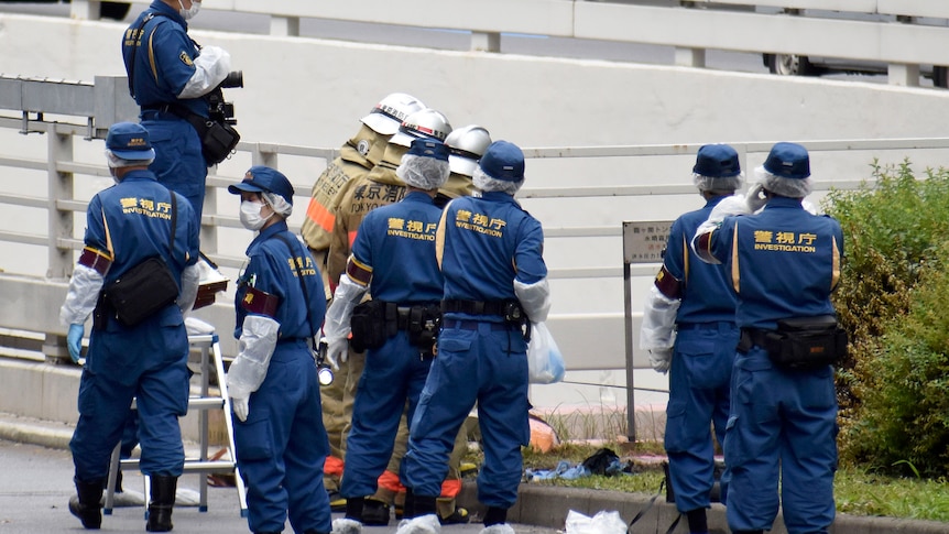 A group of men in blue jumpsuits stand around a patch of grass. 