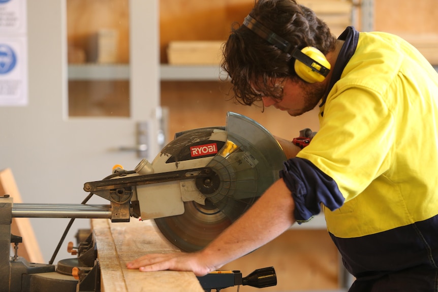 A boy cuts wood in high-vis.