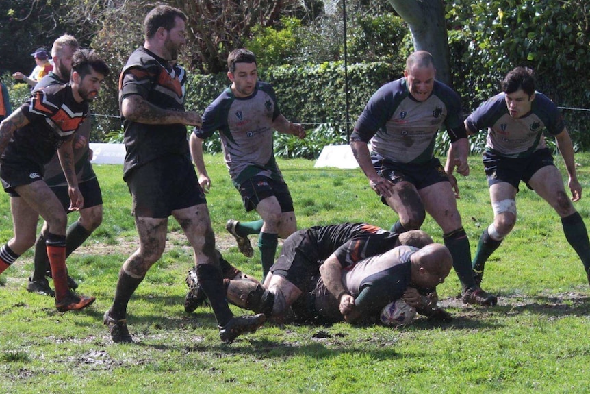 Rugby player scores a try on a muddy sporting field.