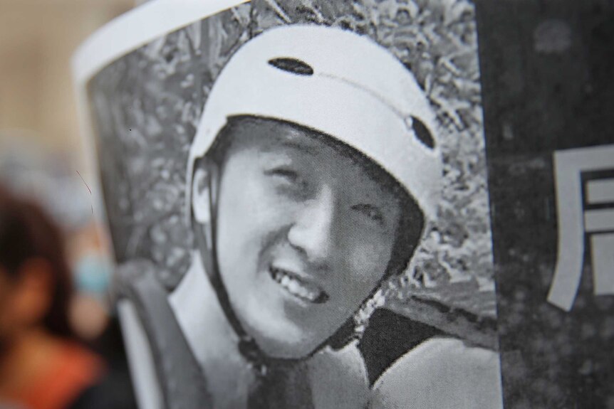 A protester holds up a black and white image of Chow Tsz-Lok, who is smiling and wearing a helmet