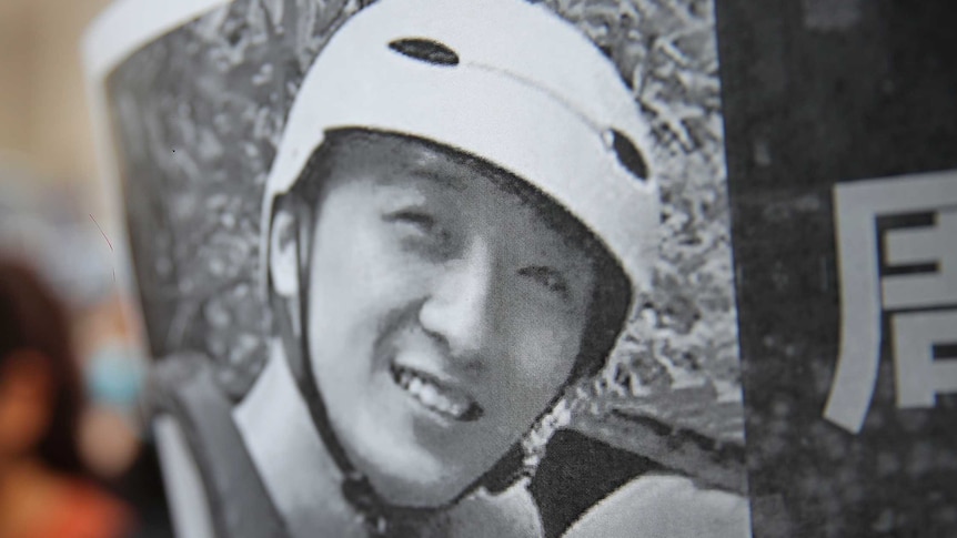 A protester holds up a black and white image of Chow Tsz-Lok, who is smiling and wearing a helmet
